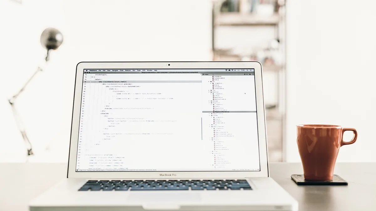 Laptop with code on screen on a clean home office desk beside a coffee cup