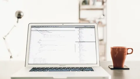 Laptop with code on screen on a clean home office desk beside a coffee cup