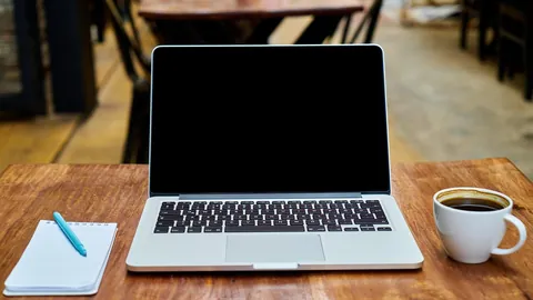 حاسوب محمول على مكتب خشبي مع دفتر وقهوة لكتابة سيرة ذاتية متوافقة مع أنظمة التوظيف