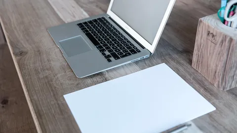حاسوب محمول وورقة بيضاء على مكتب خشبي جاهزة لكتابة نموذج سيرة ذاتية