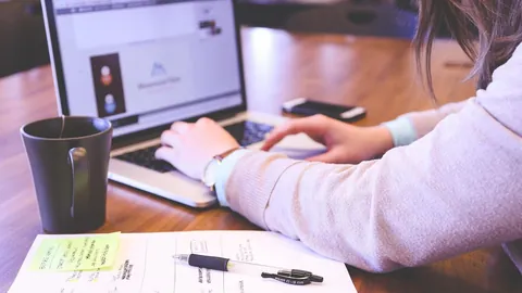 باحثة عن عمل تكتب على حاسوب محمول بجانب ملاحظات مطبوعة لتجهيز سيرتها الذاتية