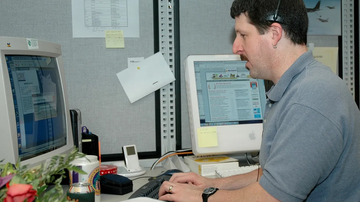 A support agent wearing a headset answers a call at his desk in a busy office
