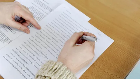 Two hands reviewing a printed page with a pen, checking the length of a letter
