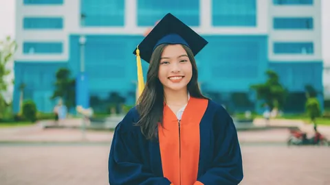 A smiling graduate in cap and gown outside her campus, ready to write a first CV with no work experience