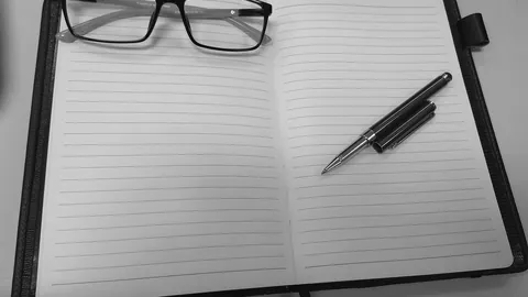 Aufgeschlagenes Notizbuch mit Brille und Kugelschreiber auf dem Schreibtisch, bereit für ein Lebenslauf Beispiel