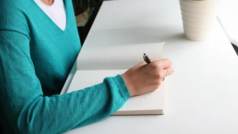 Frau schreibt an einem hellen Schreibtisch die Angaben für ihren tabellarischen Lebenslauf auf