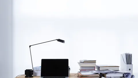 Aufgeräumter Schreibtisch mit Laptop, Lampe und Papierstapeln für die Arbeit am Lebenslauf
