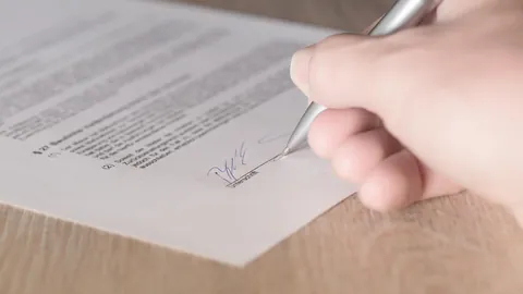 Hand unterschreibt mit Kugelschreiber am Ende eines Dokuments, wie beim Lebenslauf unterschreiben