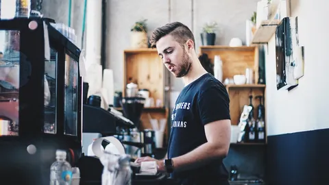 Junger Mitarbeiter bereitet an der Theke eines Cafés Getränke zu, eine typische Tätigkeit im Minijob