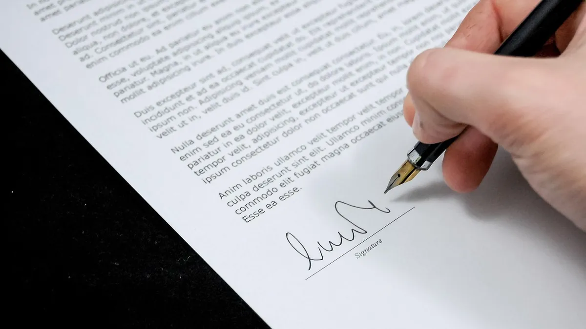 Main signant au stylo le bas d'une lettre imprimée, juste après la formule de politesse