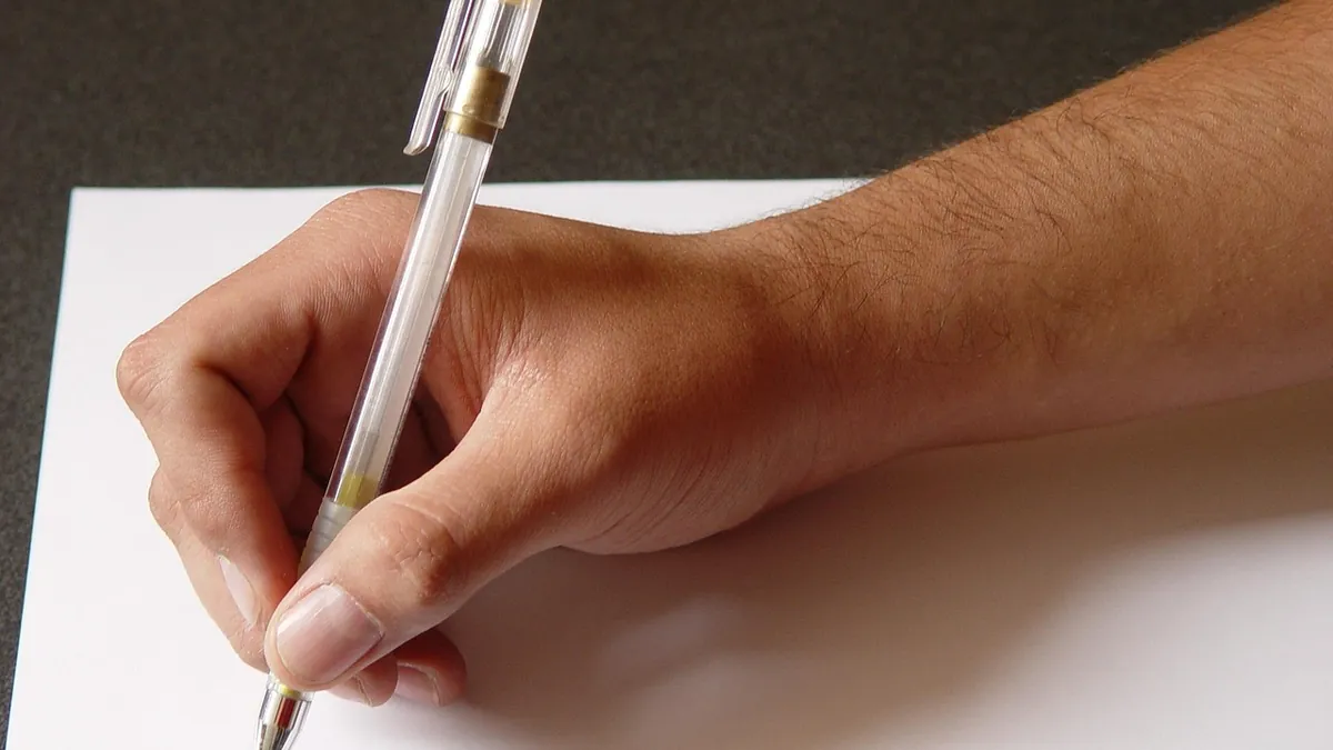 Hand holding a pen over a blank sheet, about to write a letter's opening line