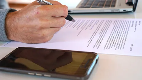 Hand writing with a pen on a printed document beside a laptop, preparing a careful job application