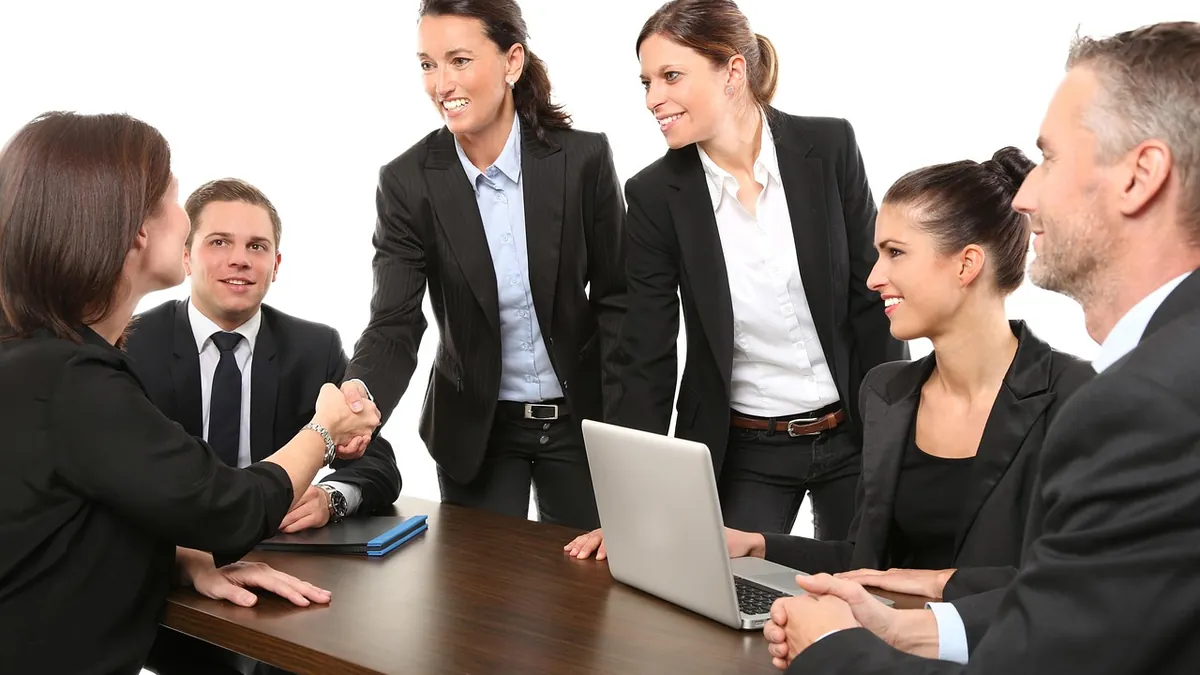 Interviewers greet a candidate with a handshake around a meeting table at the start of an HR interview