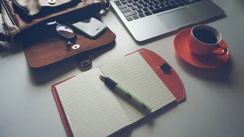 Caderno aberto, caneta, café e notebook sobre a mesa para montar um currículo simples