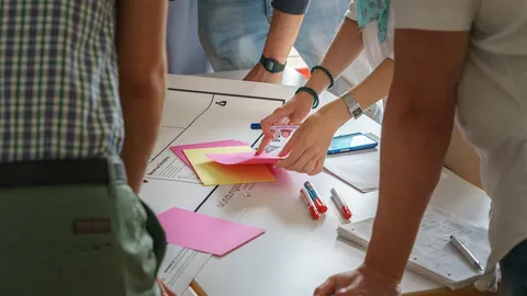 Mãos de colegas organizando notas coloridas sobre uma mesa durante uma sessão de trabalho em equipe