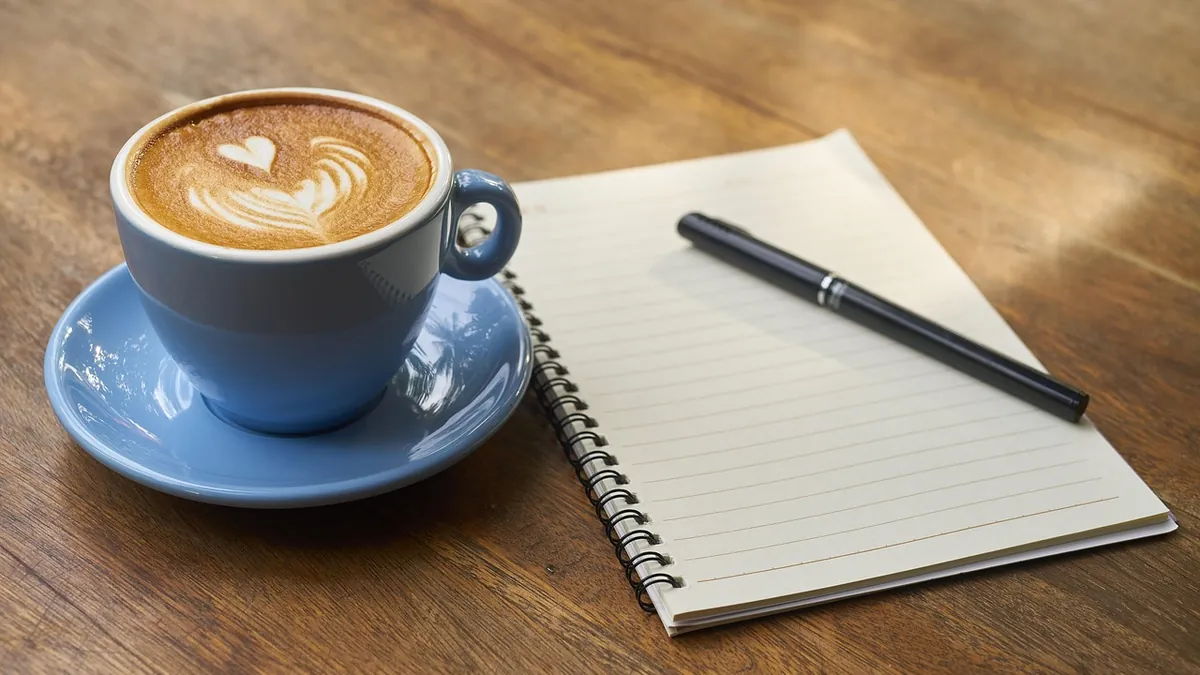 Xícara de café ao lado de um caderno em branco e uma caneta para anotar habilidades