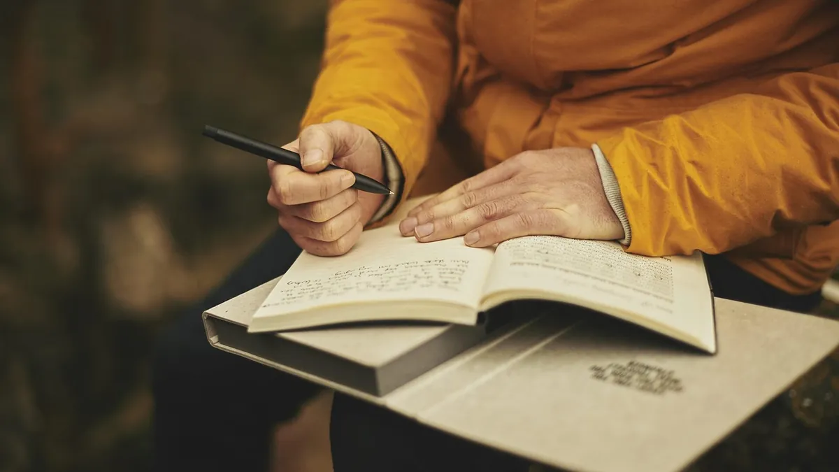 Pessoa escrevendo anotações em um caderno aberto para ajustar o seu currículo