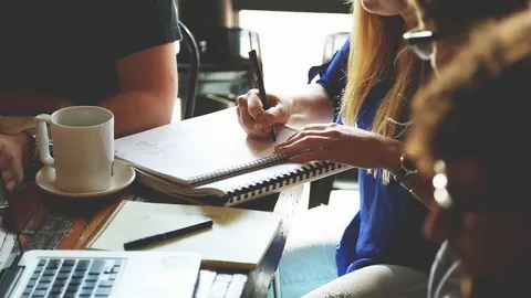 Pessoas a tomar notas num caderno à mesa enquanto planeiam objetivos profissionais