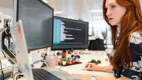 A software developer works with code on two monitors in a bright open plan office
