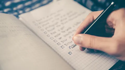 Hand writing a checklist in a notebook, listing skills to add to a resume