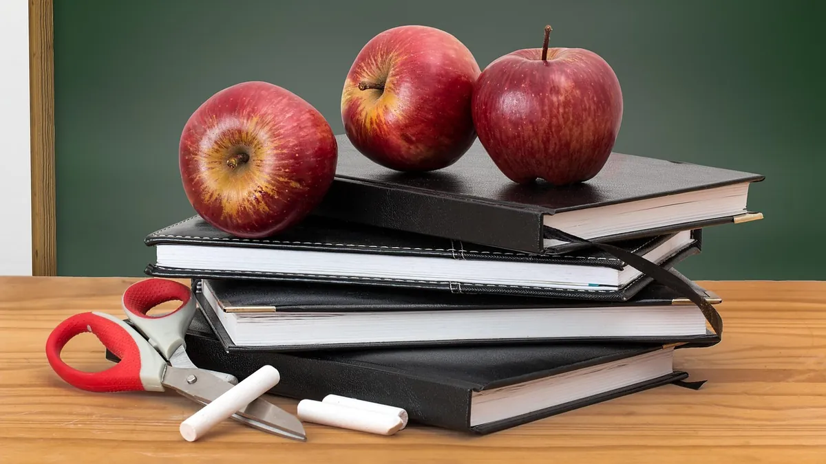 Red apples on a stack of books before a blackboard, a classic symbol of teaching